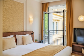 A hotel room with a bed, a television, a window with curtains, and a view of the outside.
