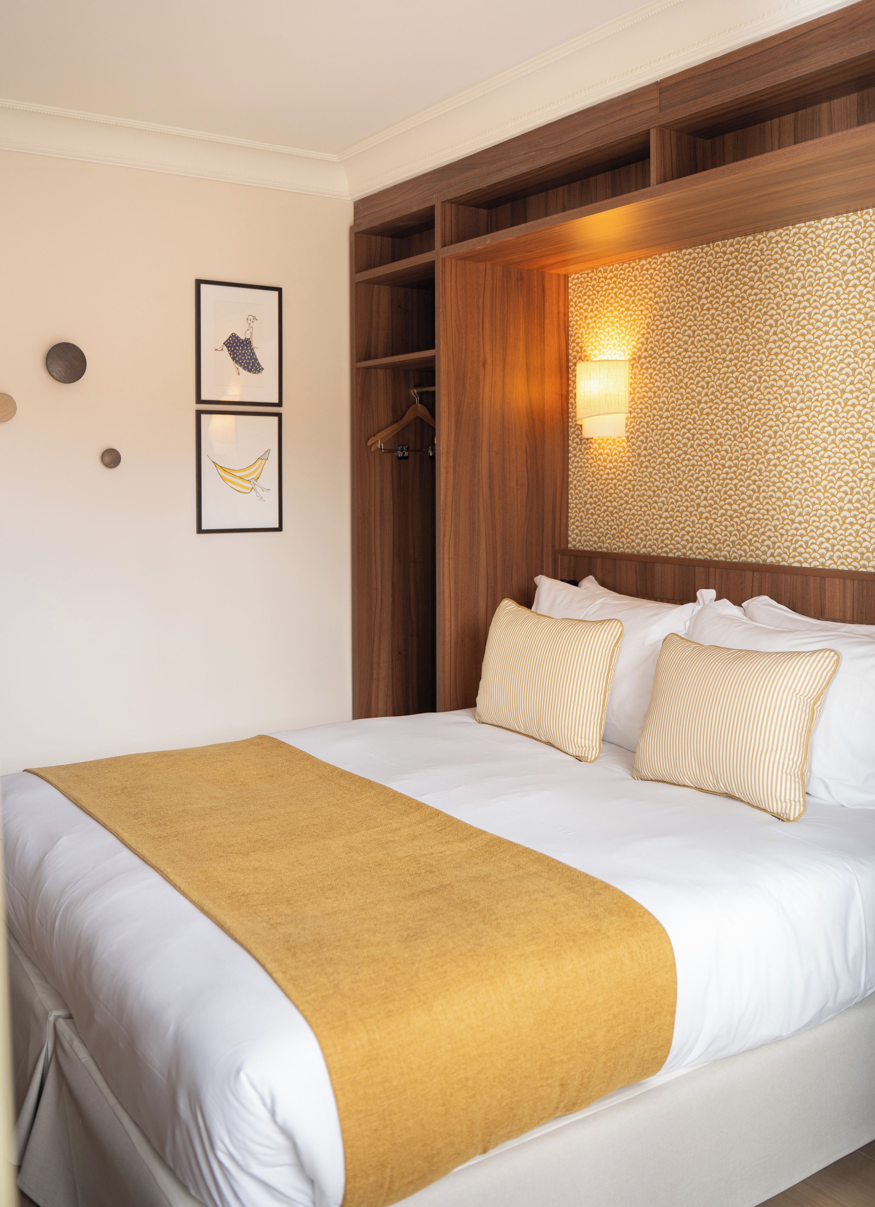 A hotel room with a bed, a wooden headboard, a wall-mounted light, and a framed picture.