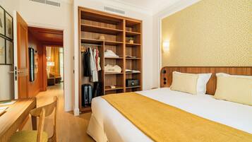 A hotel room with a bed, a wooden wardrobe, a desk with a chair, and a patterned wall.