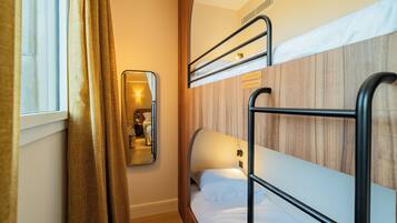 Una habitación de hotel compacta con literas, un espejo y una ventana con cortinas.