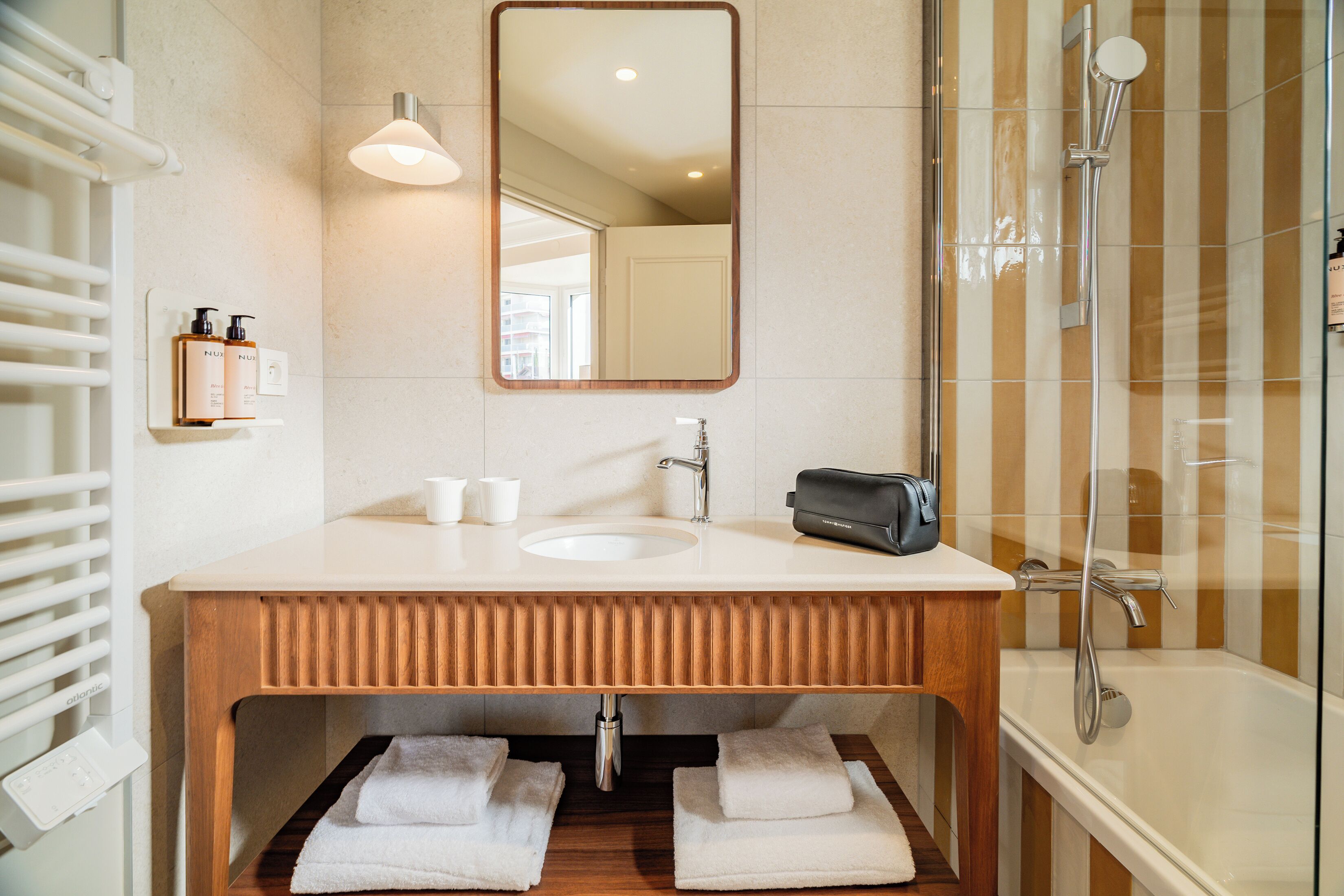 A bathroom with a wooden vanity, a mirror, a sink, a towel rack, and a shower.