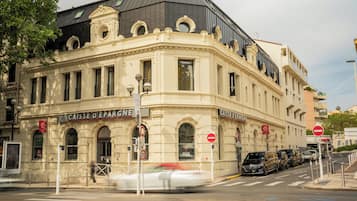Een historisch gebouw met versierde architectuur, een opvallende ingang en een straatbeeld met geparkeerde auto's en een zebrapad.