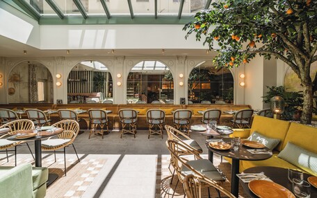 A spacious indoor area with multiple seating arrangements, including tables and chairs, and a central seating area with a sofa.