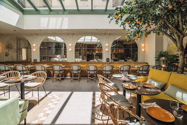 A spacious indoor area with multiple seating arrangements, including tables and chairs, and a central seating area with a sofa.