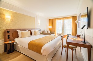 Camera d'albergo con un letto grande, una scrivania, una sedia, una lampada e una TV a parete.