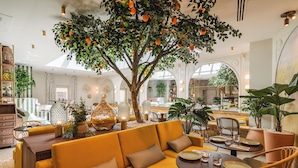 Ein modernes Interieur mit einer zentralen Sitzecke, einem Esstisch und einem großen Baum mit Orangenfrüchten.