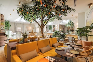 A modern interior with a central seating area, a dining table, and a large tree with oranges.