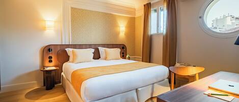 A hotel room with a bed, bedside tables, a desk, a lamp, and a window with a view.