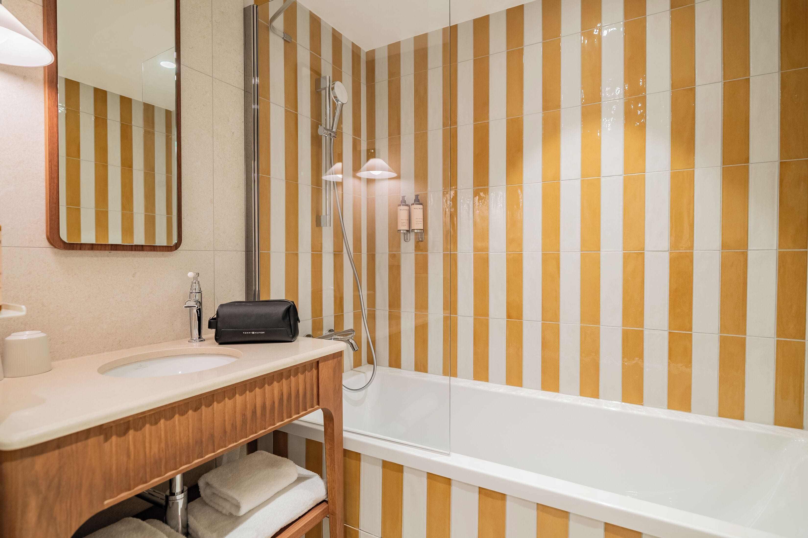 A bathroom with a bathtub, a sink, a mirror, and striped wall tiles.