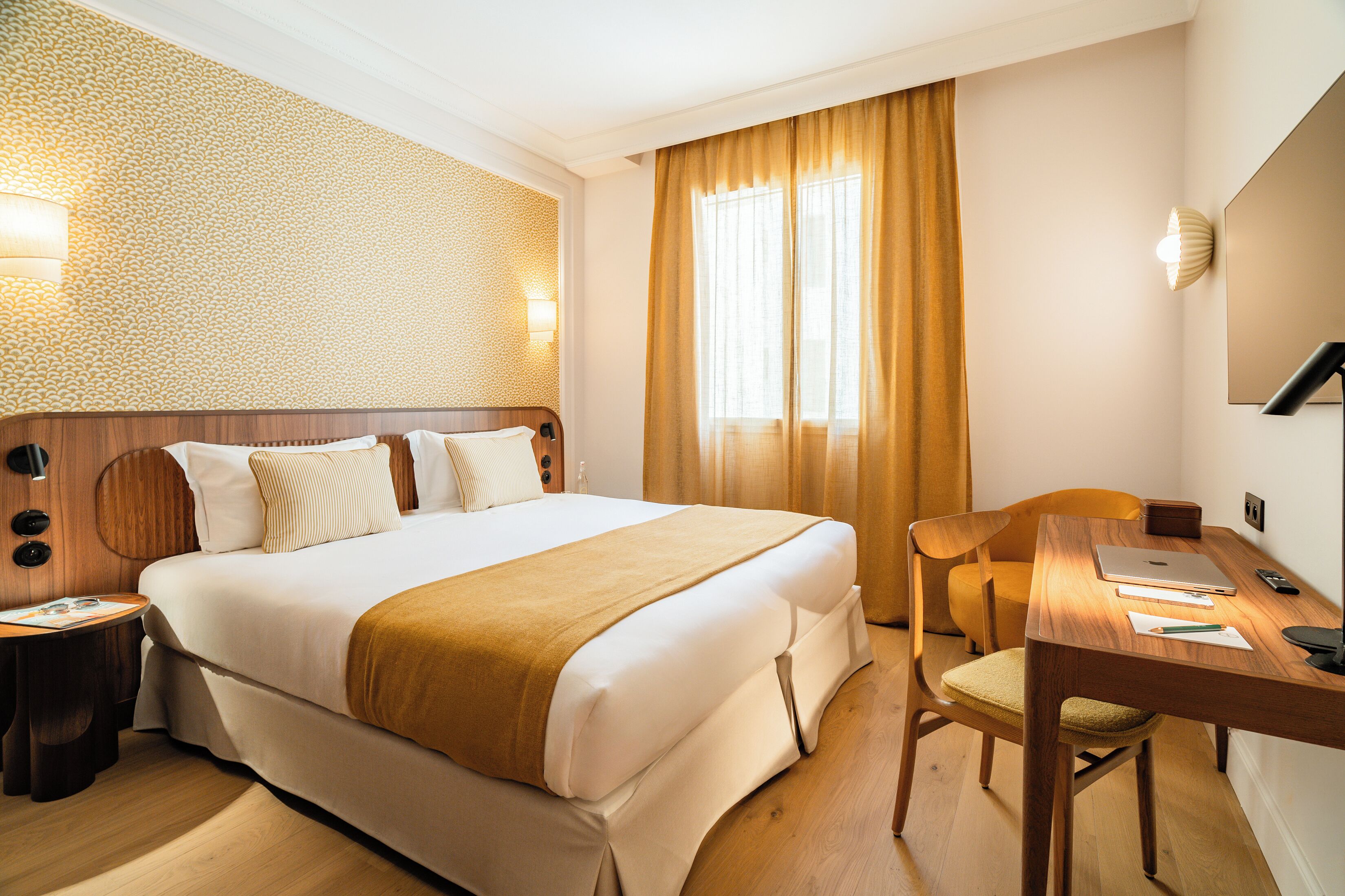 A hotel room with a large bed, a desk, a chair, a lamp, and a wall-mounted light.