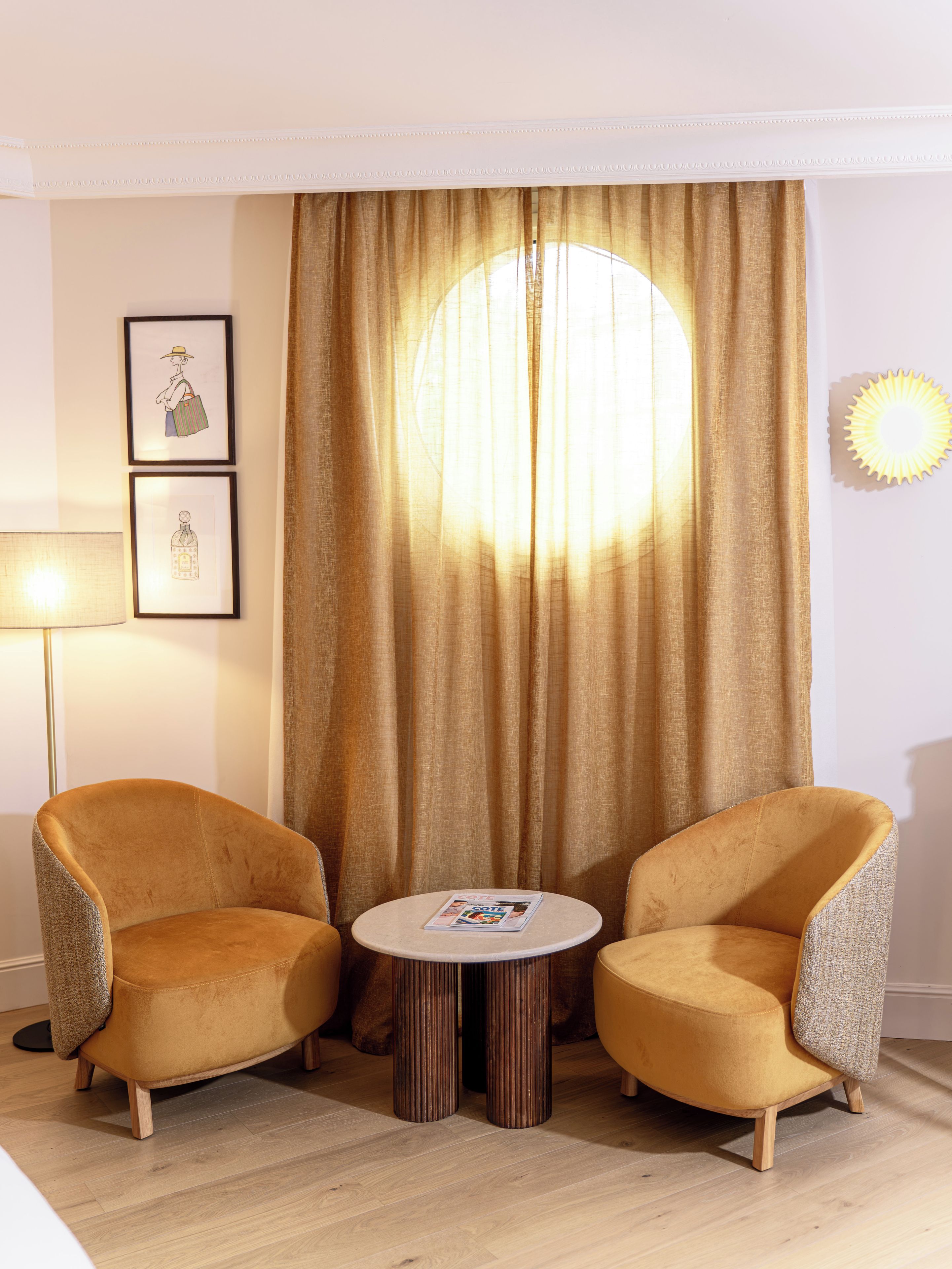 Quarto com duas poltronas, uma mesinha redonda, luminária de chão e uma grande janela com cortinas.