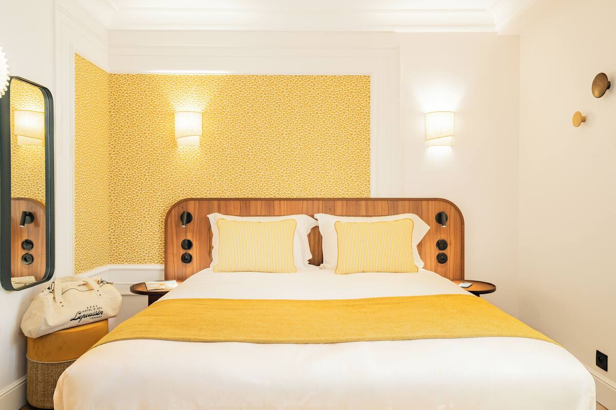 A hotel room with a bed, a nightstand, a lamp, a mirror, and a patterned wall.