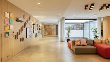 Un moderno vestíbulo de hotel con un largo pasillo, un sofá modular y una pared decorada con diversos objetos enmarcados.