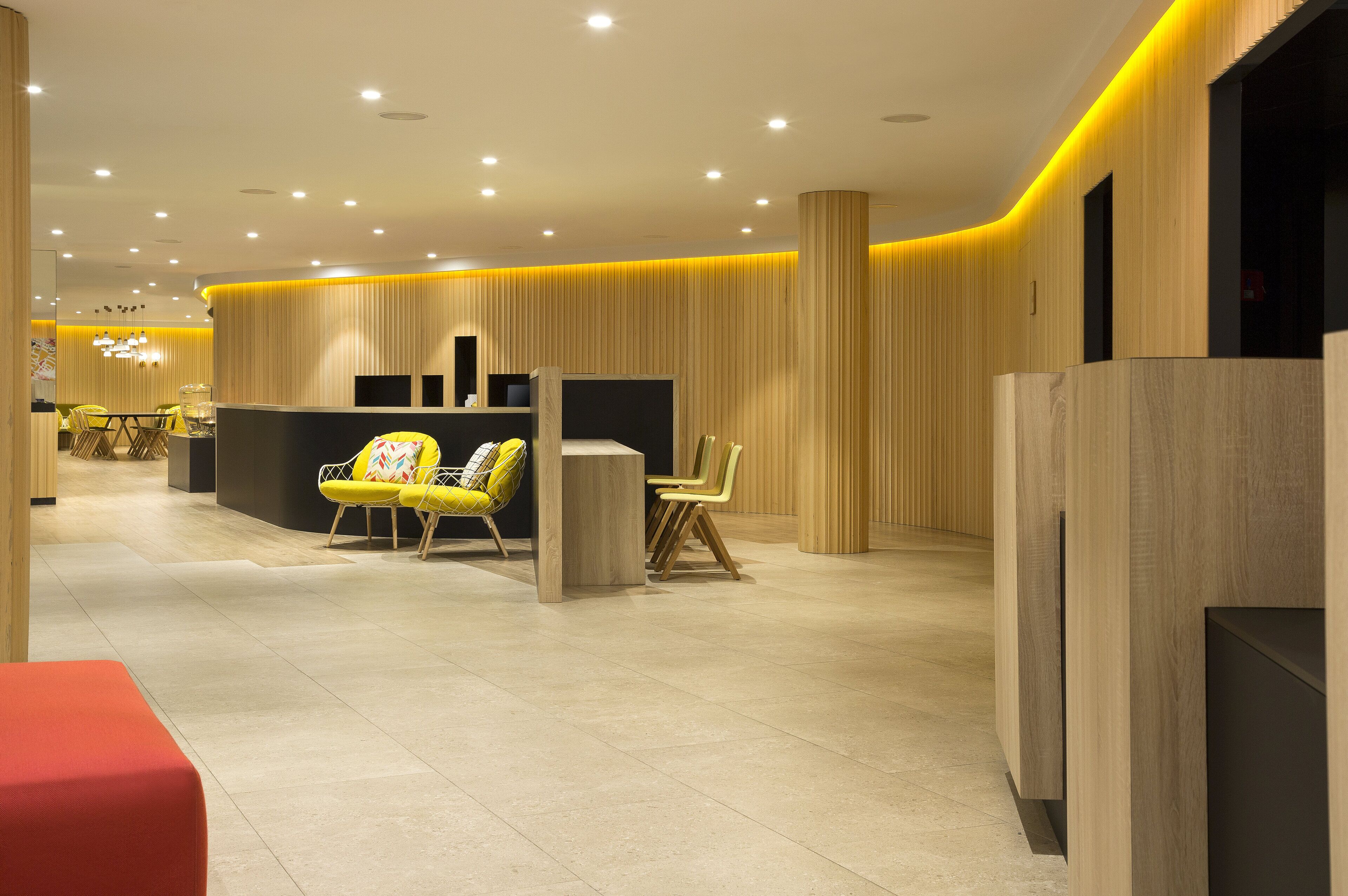 A modern hotel lobby with a reception desk, yellow chairs, and a red bench.
