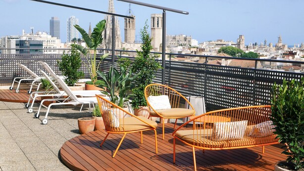 A rooftop terrace with wooden flooring, white lounge chairs, and orange wicker chairs. - Citadines Ramblas Barcelona (Barcelona)