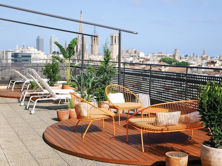 A rooftop terrace with wooden flooring, white lounge chairs, and orange wicker chairs.