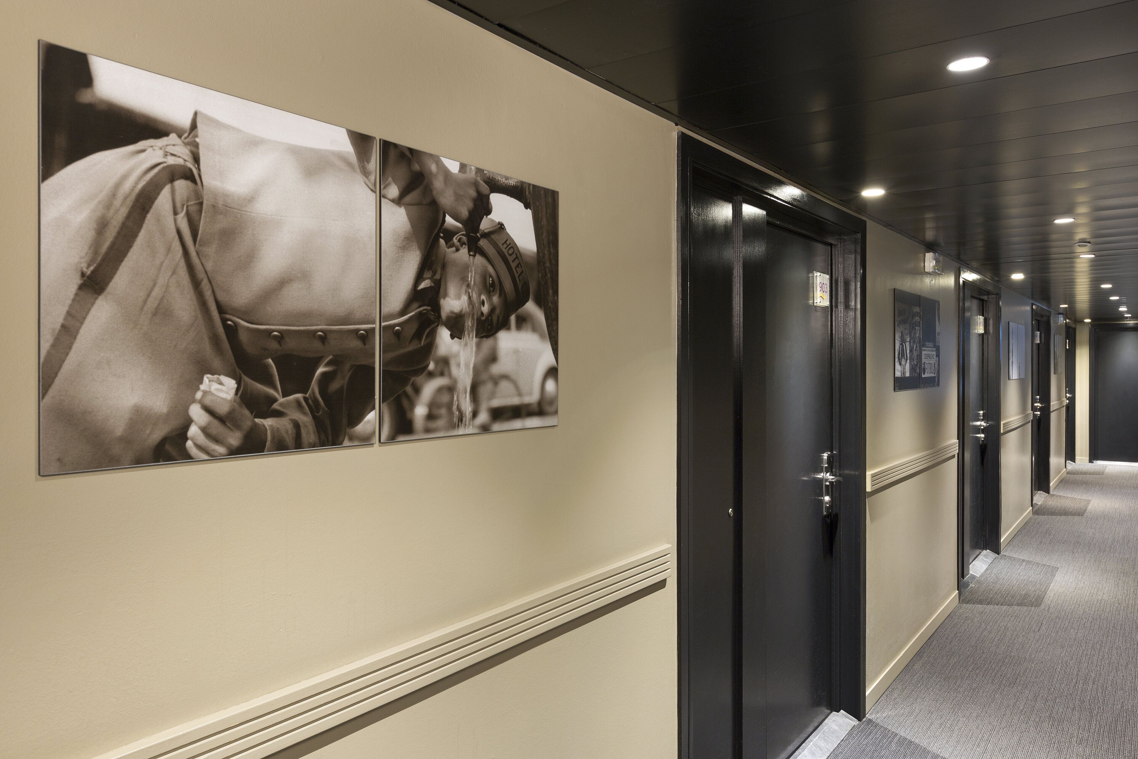 Un pasillo de hotel con varias puertas, una alfombra estampada y una fotografía colgada en la pared.