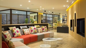 A modern living area with a sofa set, two round tables, and a large TV screen. - Citadines Ramblas Barcelona (Barcelona)