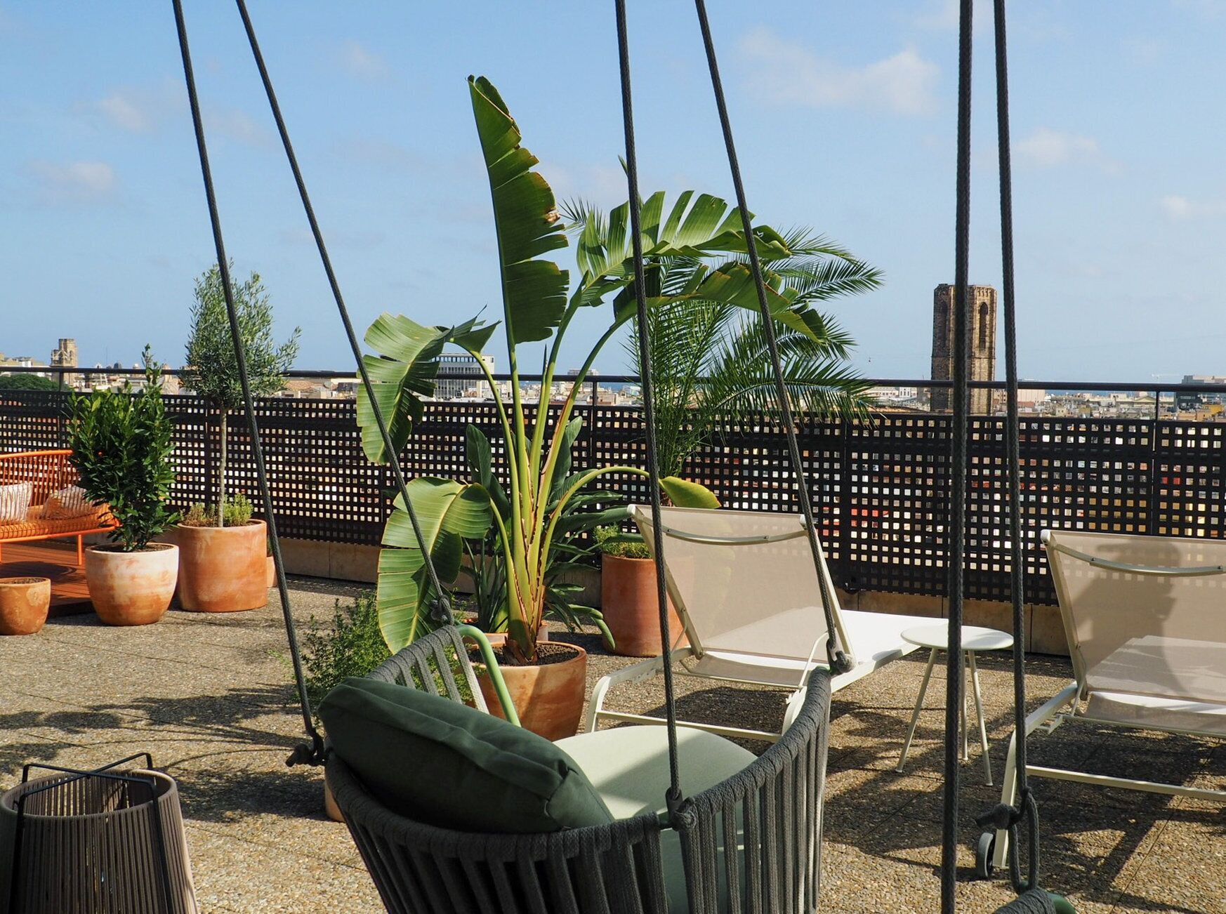 Eine Dachterrasse mit einer Schaukel, einem gepolsterten Sessel und mehreren Blumentöpfen.