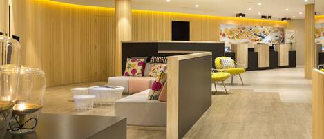 A modern reception area with a wooden reception desk, a sofa with colorful cushions, and a yellow chair.