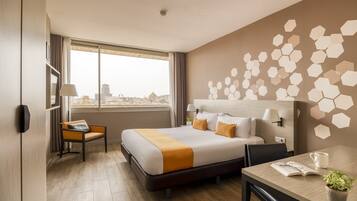 Quarto de hotel com cama, escrivaninha, cadeira, janela e vista da cidade.