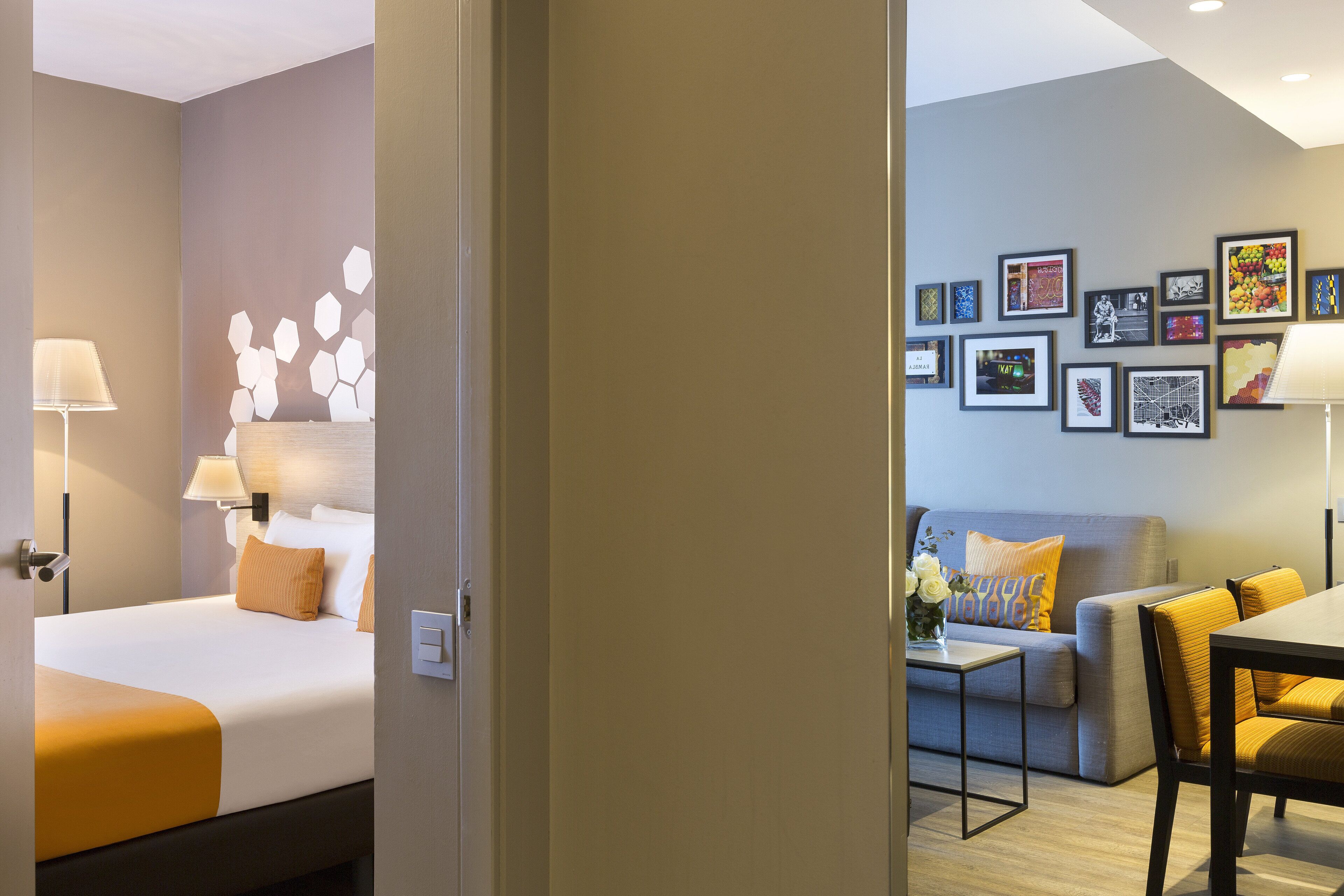 A hotel room with a bed, a sofa, a dining table, and a wall decorated with framed pictures.