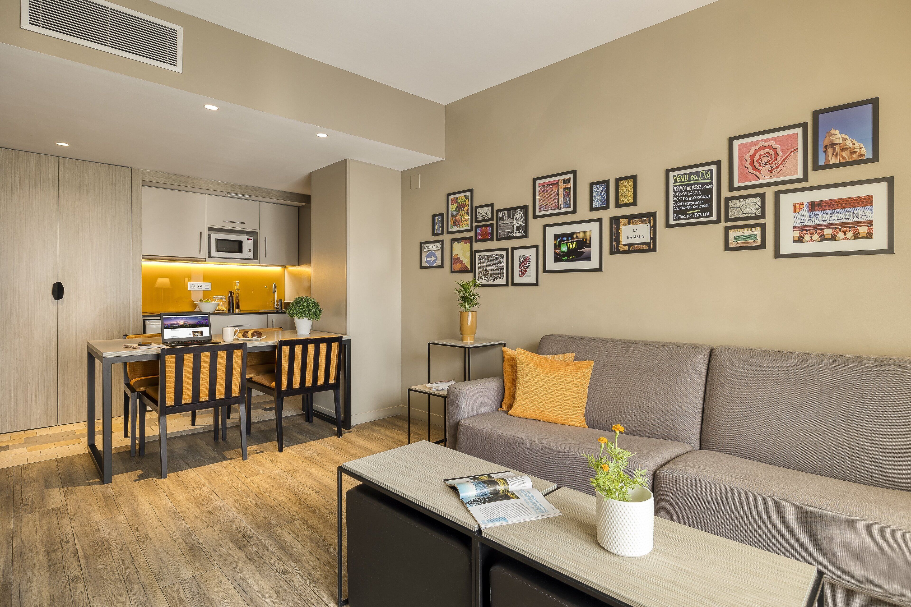 A modern living room with a grey sofa, a dining table with chairs, and a kitchen area with a microwave.