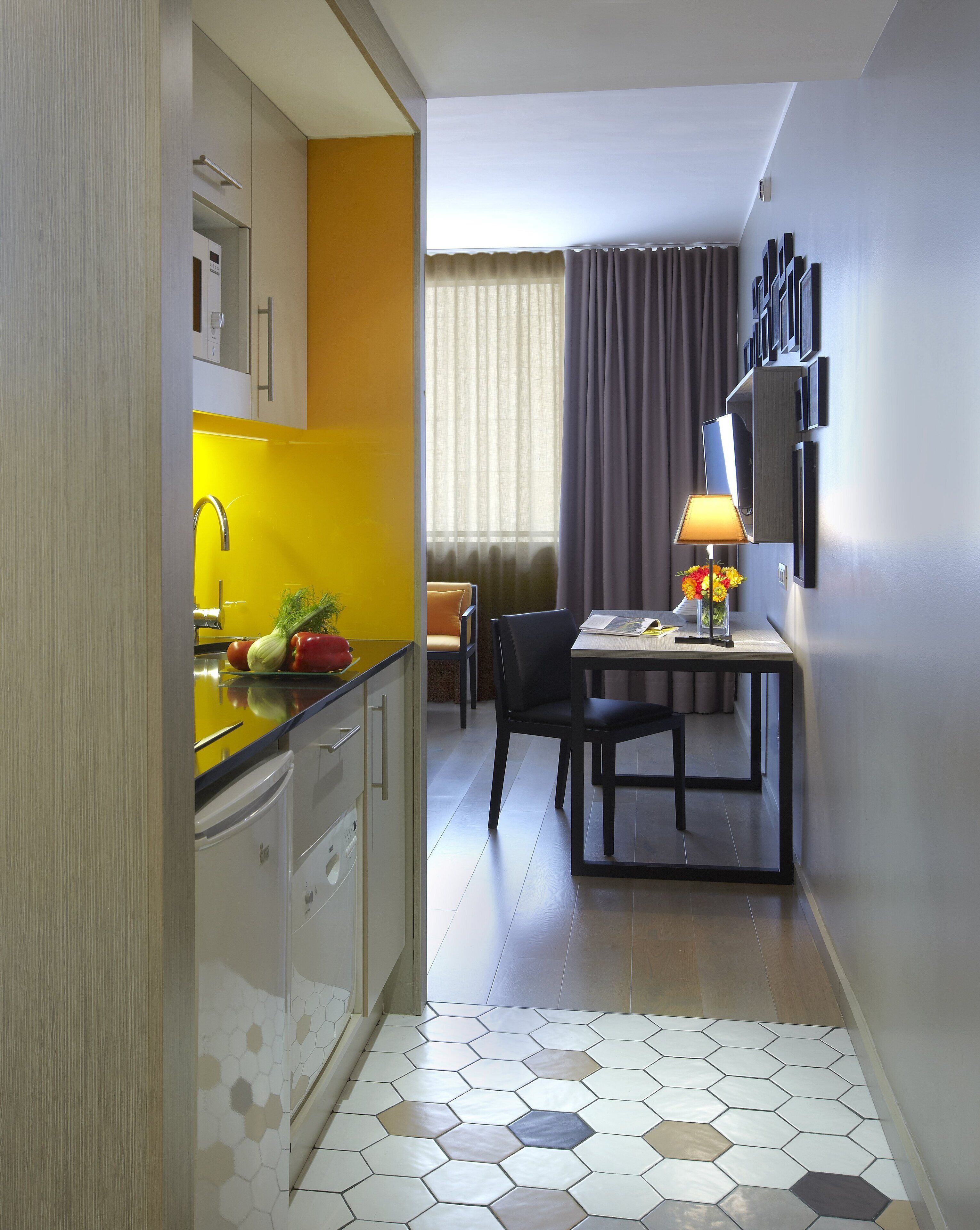 Una habitación de hotel compacta con cocina, comedor y un gran ventanal con cortinas.