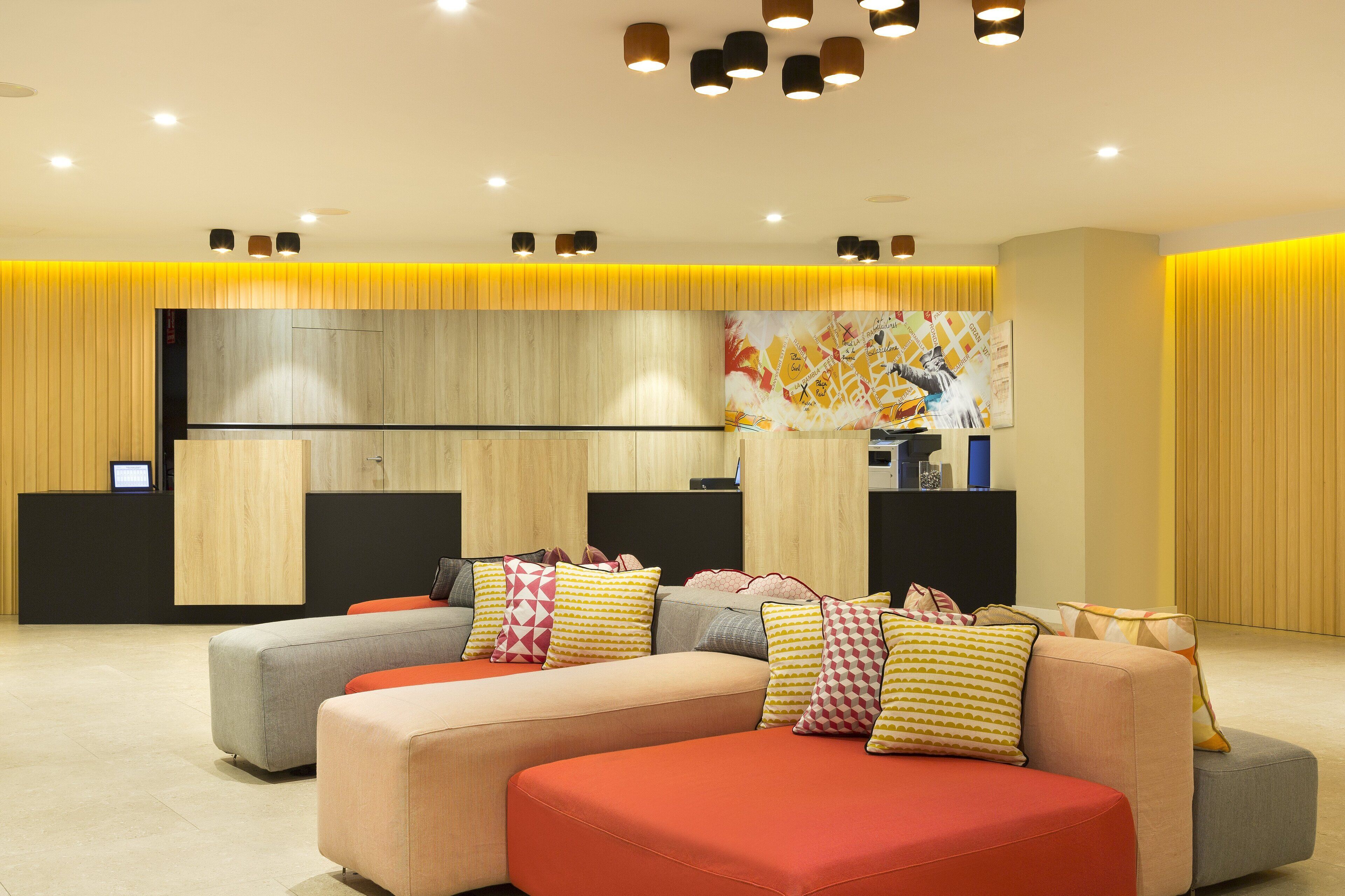 A modern hotel lobby with a reception desk, a large sectional sofa with colorful cushions, and a contemporary art piece on the wall.
