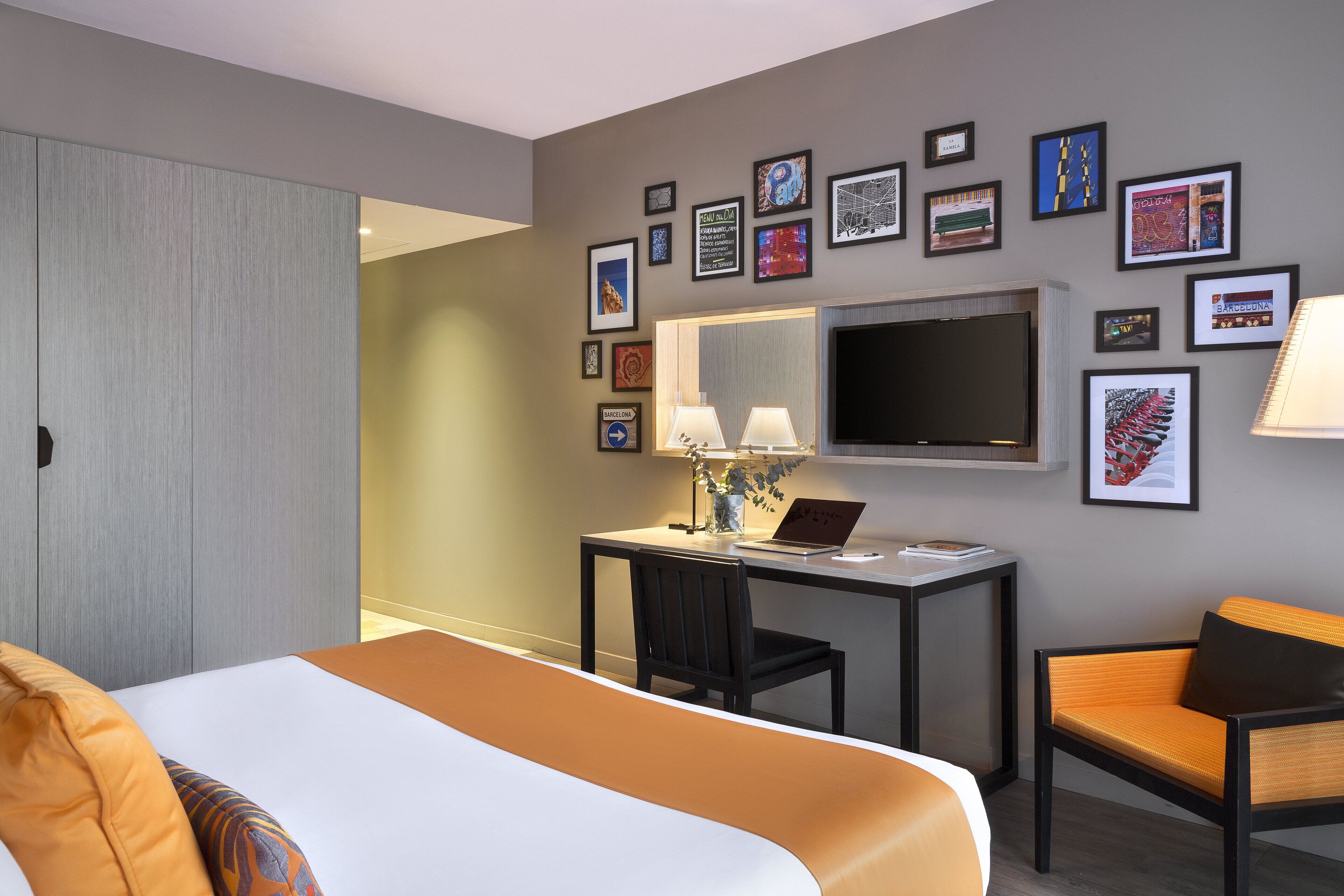 A hotel room with a bed, desk, chair, TV, and wall art.