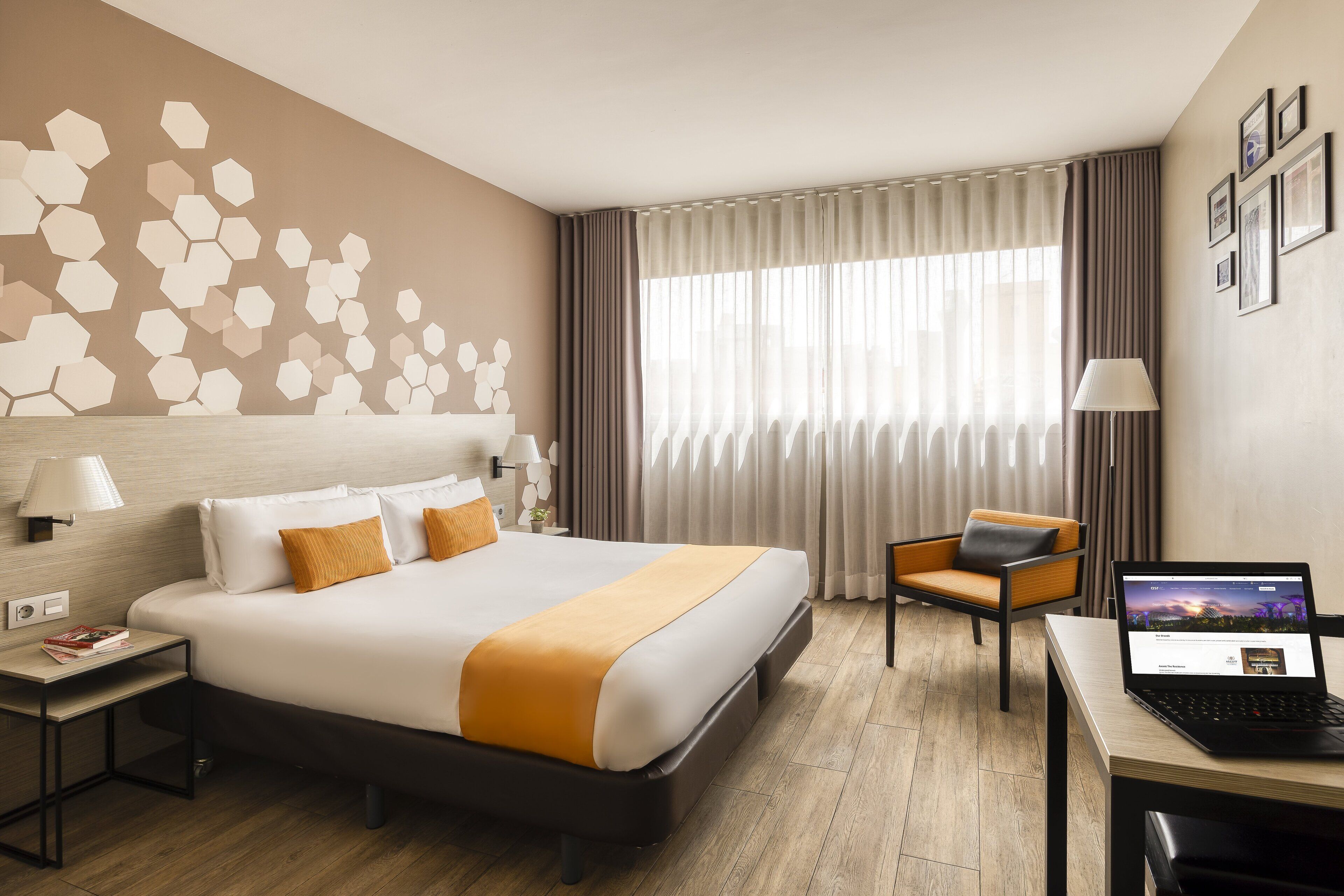 Habitación de hotel con cama, escritorio con una computadora portátil, una silla, mesita de noche y pared con diseños hexagonales.