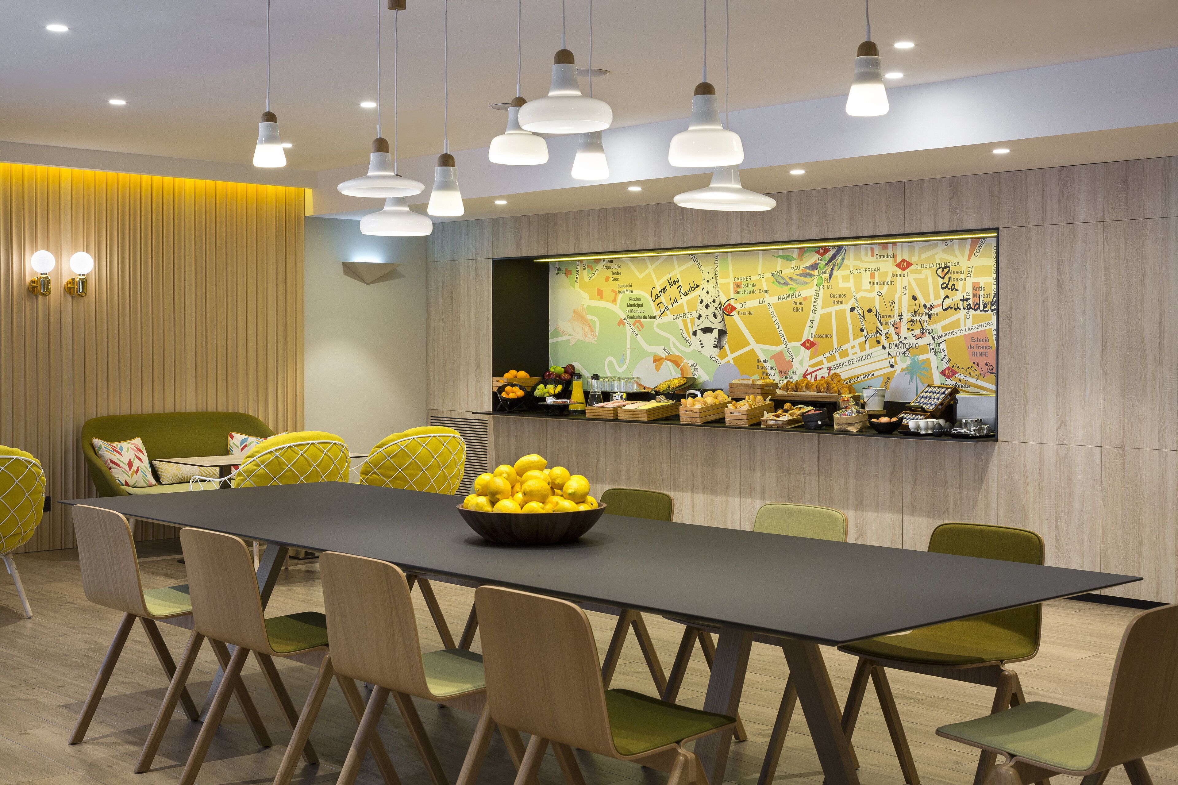 A modern dining area with a long table, green chairs, and a bowl of lemons.