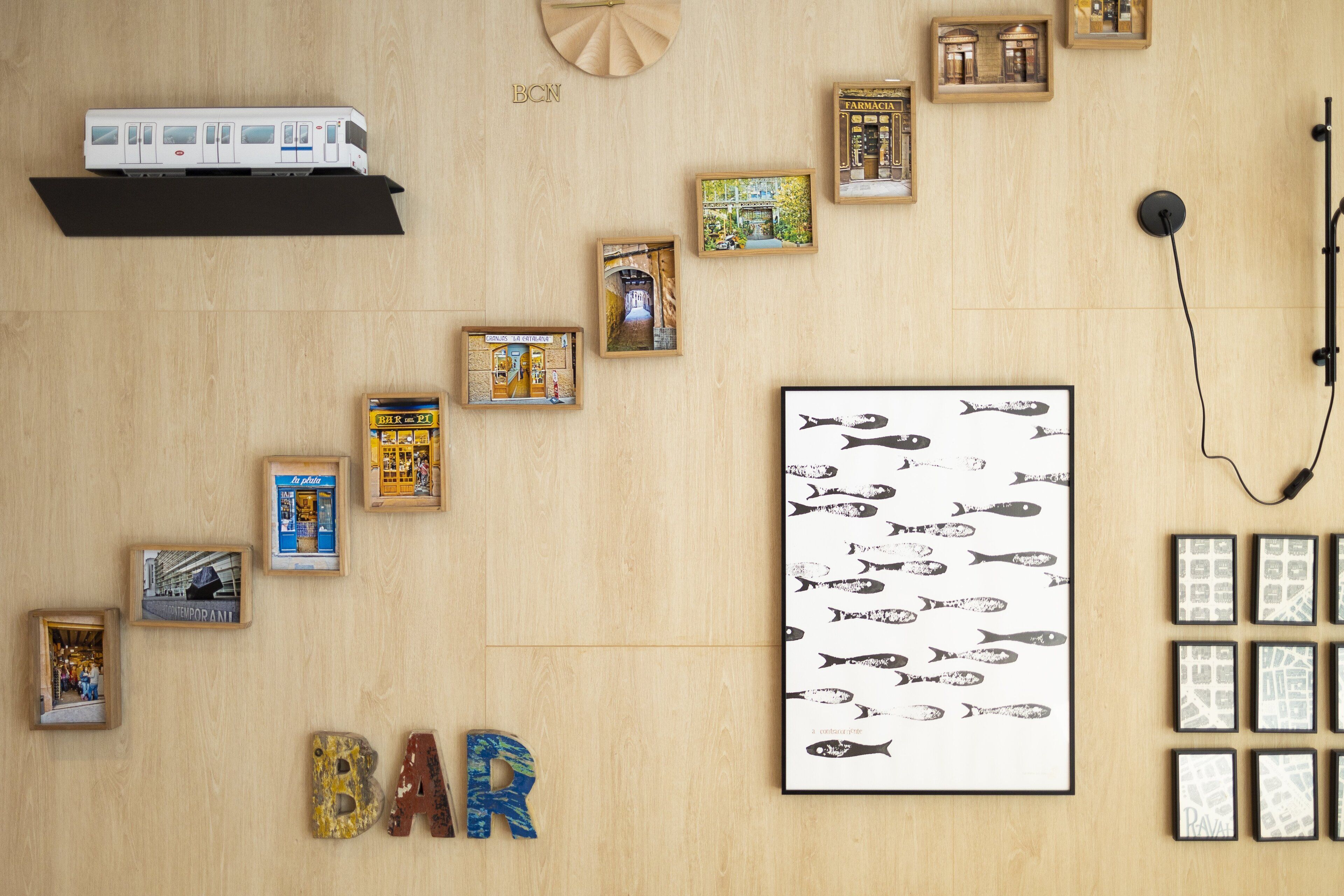 A room with a wooden floor, a mounted shelf with a model train, several framed pictures, and a large framed fish pattern.