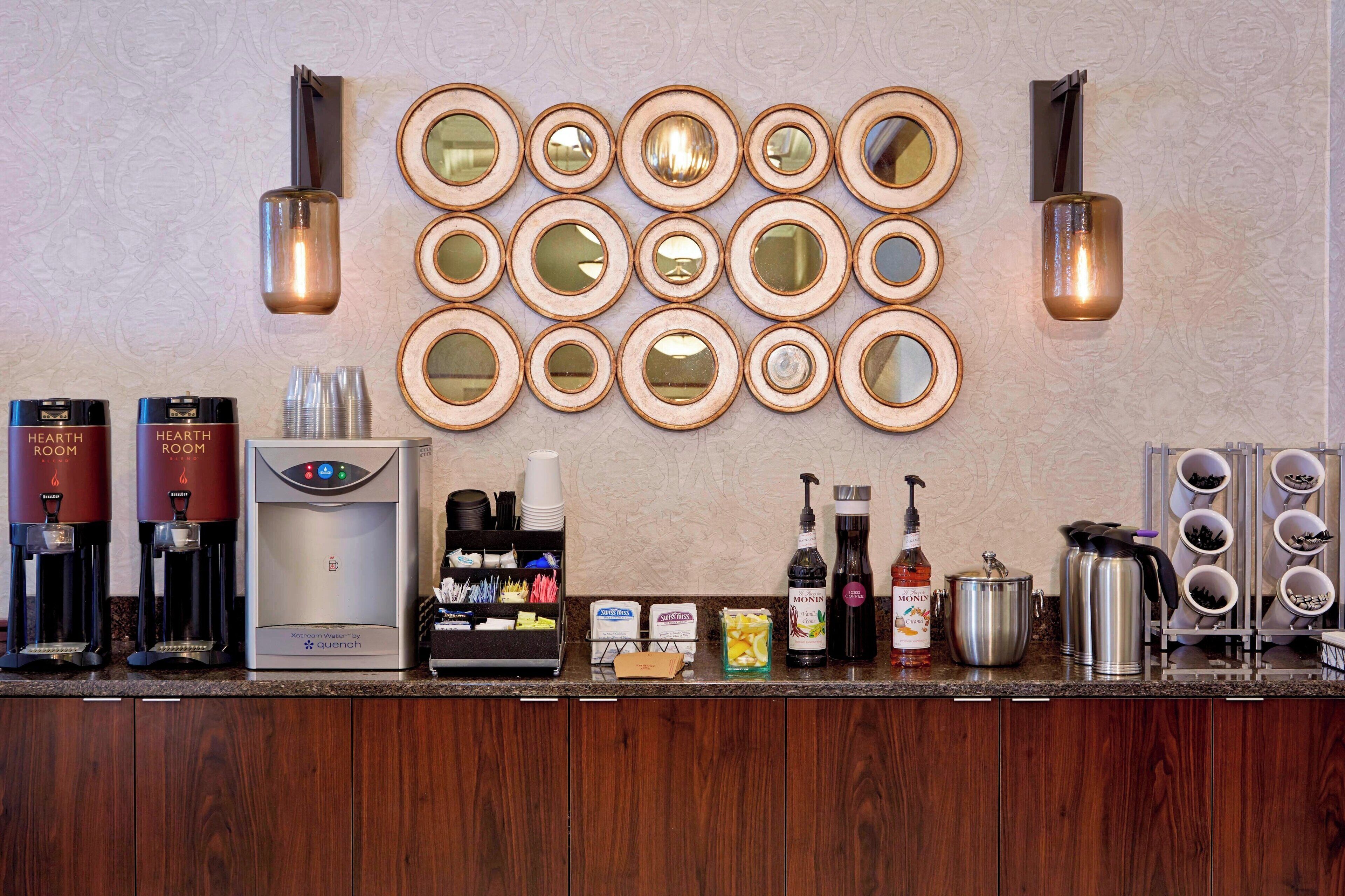 Un espace bar dans l’hôtel, équipé de machines à café, d’un distributeur d’eau, ainsi que de divers condiments et ustensiles.