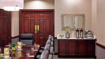 A conference room with a long table, leather chairs, a coffee station, and a large mirror on the wall.
