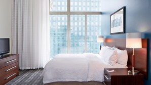 A hotel room with a large window, a bed with white linens, a wooden nightstand with a lamp, and a television on a dresser. - Residence Inn Milwaukee Downtown by Marriott (Milwaukee)