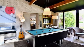 A pool table in a room with a brick wall, a guitar, and a piano.
