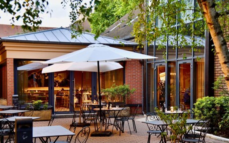 An outdoor cafe area with tables and chairs, umbrellas, and potted plants.