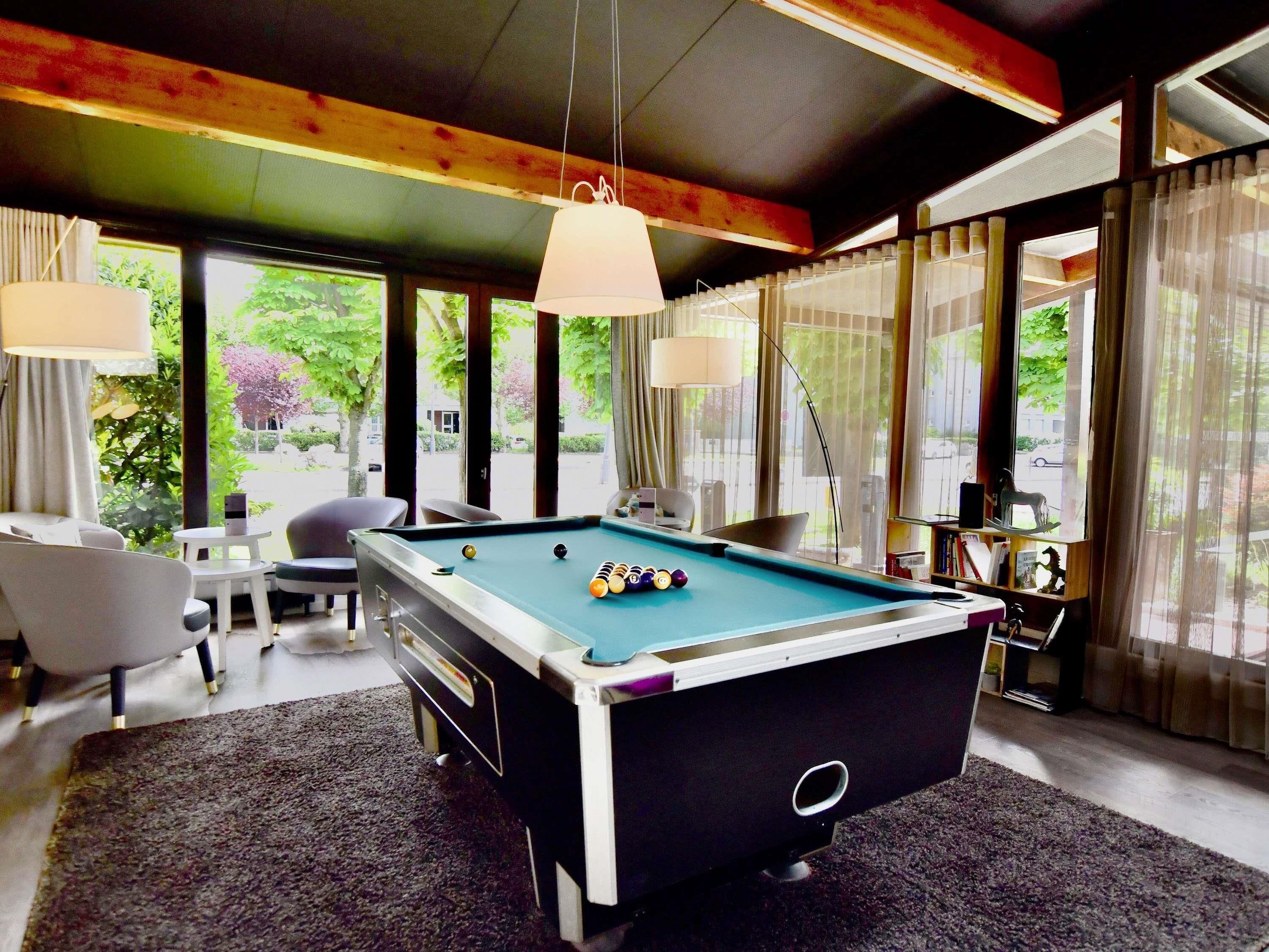 A pool table in a room with large windows, a sofa, and a lamp.