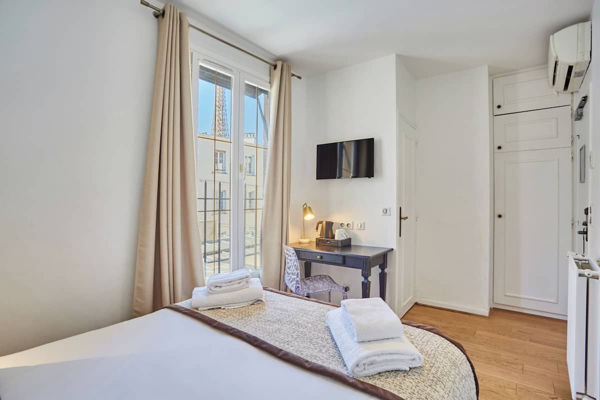 A hotel room with a bed, a desk, a chair, a television, and a wardrobe.