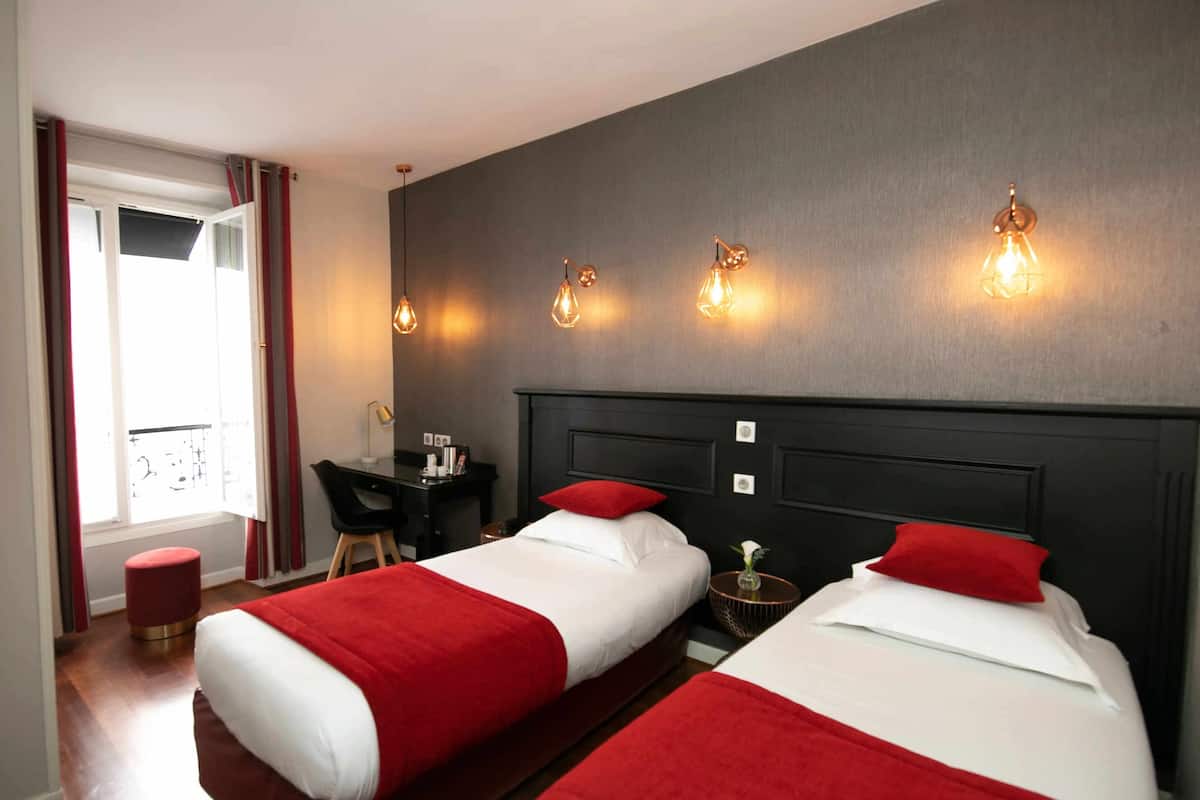 A hotel room with two beds, a desk, a chair, and a small stool.