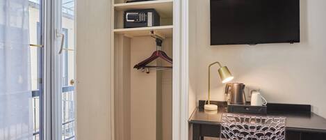 A room with a desk, a hanging TV, a coat rack, and a window.