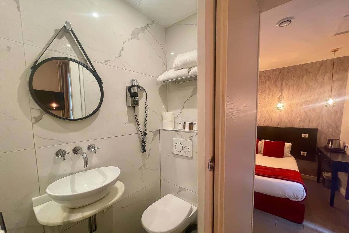 A modern bathroom with a sink, toilet, and bidet. There is a mirror, a towel rack, and a hairdryer on the wall.