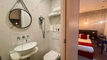 A modern bathroom with a sink, toilet, and bidet. There is a mirror, a towel rack, and a hairdryer on the wall.