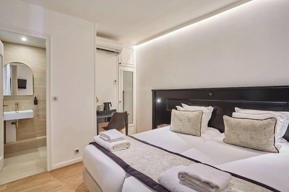 A hotel room with a large bed, a bedside table, a mirror, and a bathroom visible through an open door.