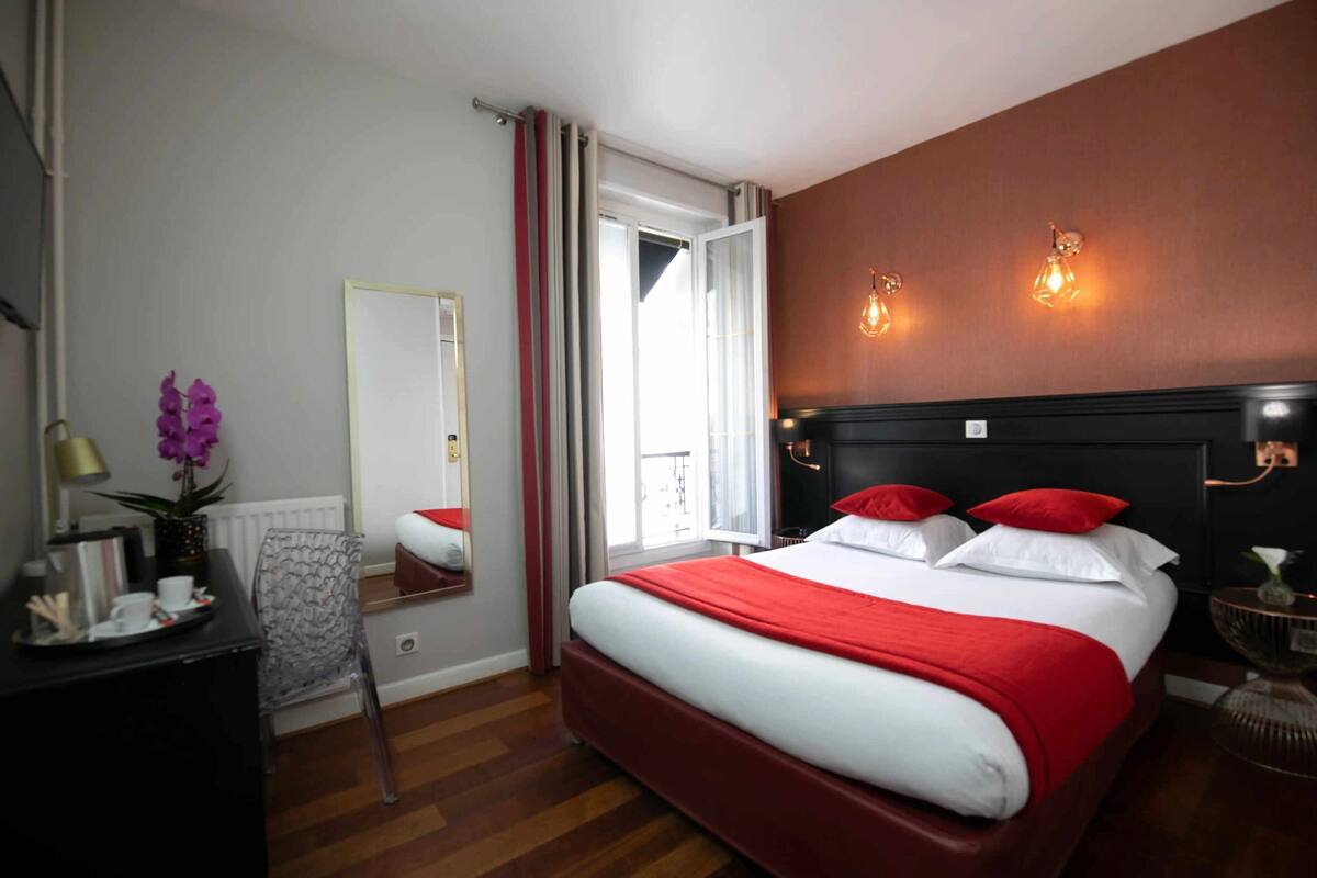 A hotel room with a bed, a desk, a chair, a mirror, and a window.