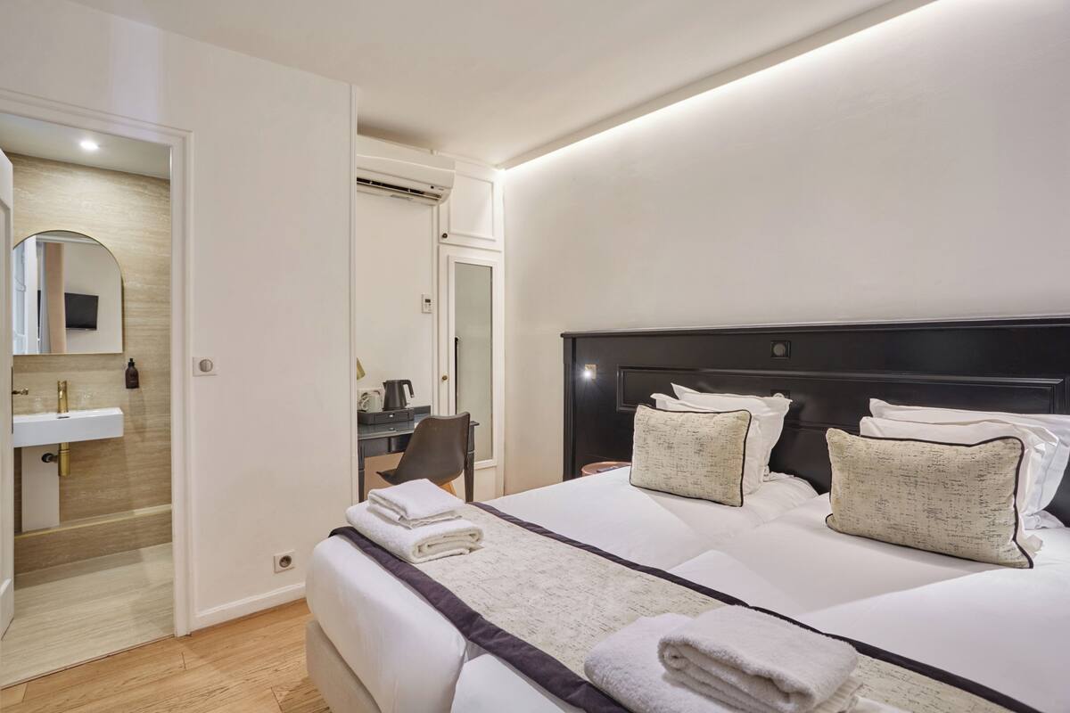 A hotel room with a bed, a desk, a chair, a mirror, and a bathroom.