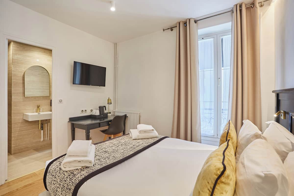 A hotel room with a bed, a desk, a TV, a bathroom, and a view of the outdoors.