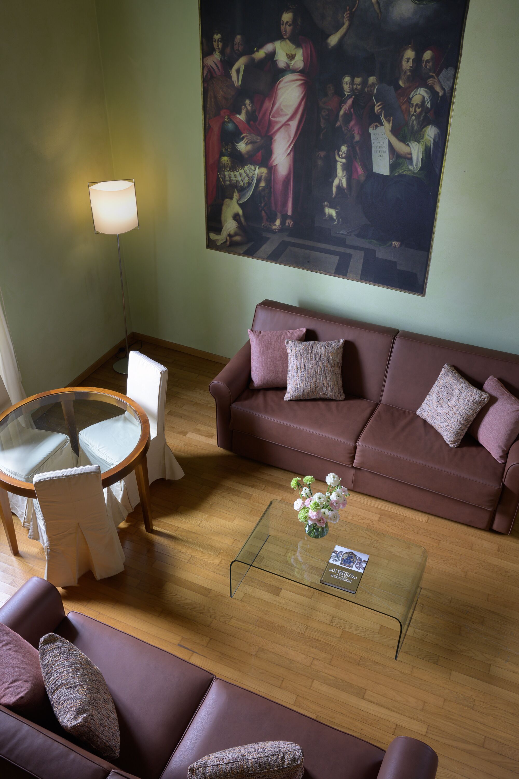 A living room with a brown sofa, a glass coffee table, and a painting on the wall.