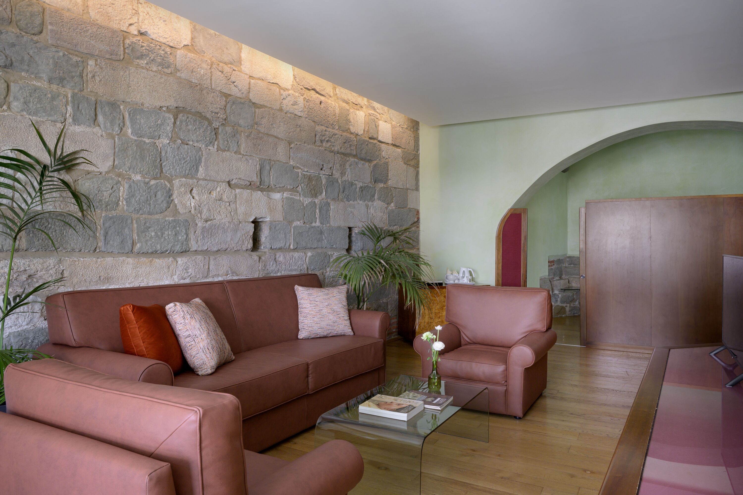 A living room with a stone wall, a brown leather sofa, a glass coffee table, and a wooden cabinet.